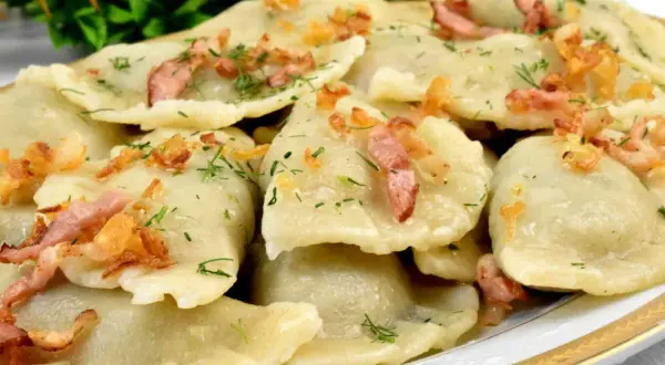 Talerz pełen pysznych, domowych pierogów z młodej kapusty, posypanych skwarkami i koperkiem.