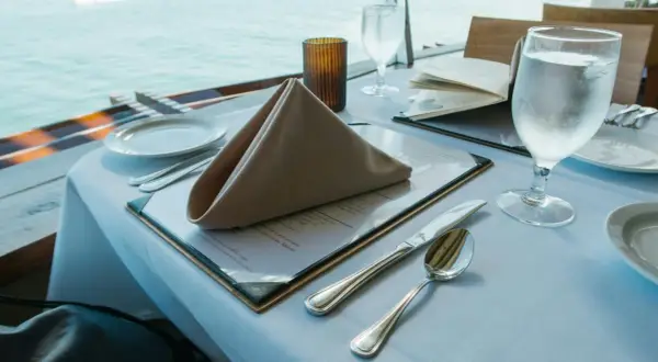Stół w restauracji z widokiem na morze, nakryty do posiłku, z menu i kieliszkiem wody.