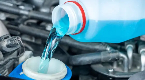 Blaues Scheibenwischwasser wird aus einem Behälter in den Einfüllstutzen gegossen.