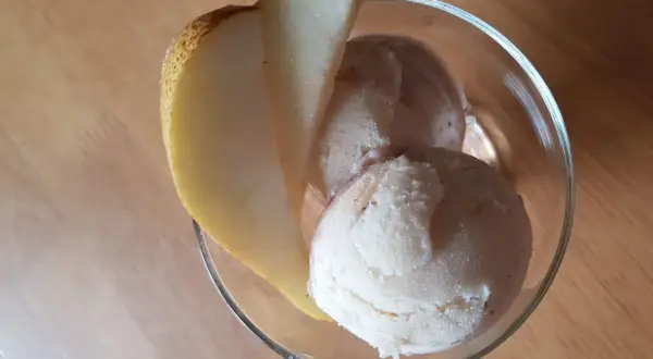 Ein Glas mit cremigem birnen eis, garniert mit einer frischen Birnenspalte, steht auf einem Holztisch.