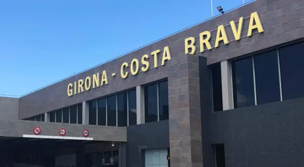 Złote litery "GIRONA - COSTA BRAVA" na nowoczesnym budynku lotniska.