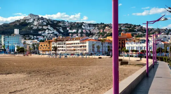 Playa de Peñíscola con el paseo marítimo y edificios blancos escalonados en la ladera de una montaña.