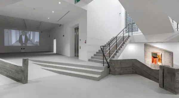 Wnętrze muzeum sztuki współczesnej Kraków: projekcja wideo, betonowe schody i rzeźba.