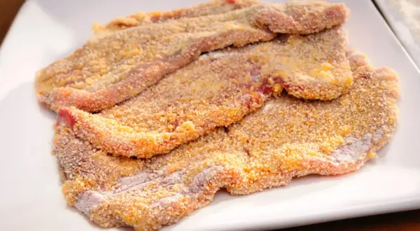 Mehrere panierte Schnitzel liegen auf einem weißen Teller, bereit für ein köstliches Schnitzel Rezept.