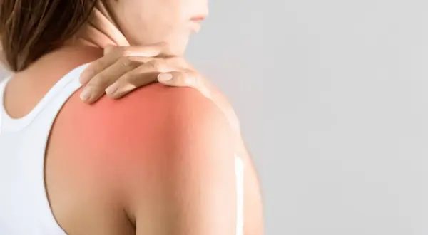 En person håller sin axel där en röd fläck indikerar muskelinflammation i armen.