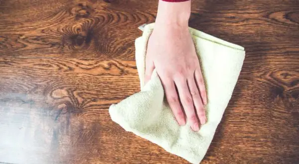 Mano limpiando un suelo de madera con un paño, aprendiendo como quitar manchas de la madera sin dañarla.