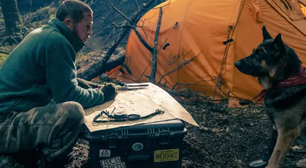 Man och hund vid orange tält, planerar en expedition. Kanske är det hjärtat av besten de söker.