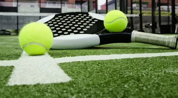 Raqueta de pádel y pelotas sobre césped artificial padel. La cancha está lista para el juego.