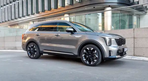 Elegancka, szara nowa Kia Sorento z czarnymi felgami stoi przed nowoczesnym budynkiem.
