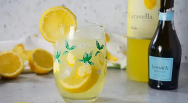 En uppfriskande limoncello spritz med citronklyftor i ett glas med citrontryck. Bredvid står en flaska prosecco och en flaska limoncello.
