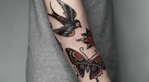 Tatuaż w stylu old school na przedramieniu: jaskółka, motyl i róża.