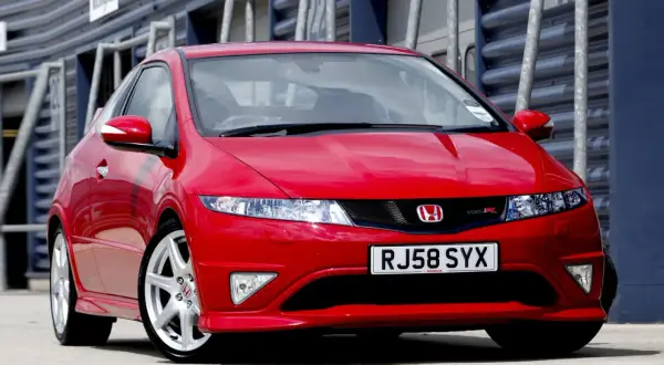 Czerwony Honda Civic Type R, wyglądający jak futurystyczne UFO, zaparkowany na torze wyścigowym.