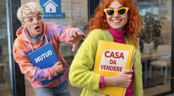 Ragazza sorridente con cartella "CASA DA VENDERE" e ragazzo spaventato con cartella "MUTUO" fuori da un'agenzia immobiliare.