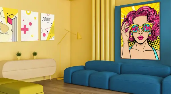 Nowoczesny salon z niebieską kanapą i żółtymi akcentami. Na ścianie wiszą kolorowe pop art obrazy, w tym portret kobiety w okularach.
