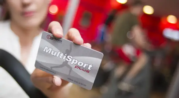 Karta MultiSport Plus w ręce na tle siłowni.