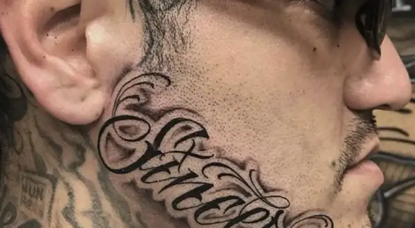 Wyrazisty tatuaż na twarzy z napisem "Sincere" w ozdobnej czcionce.