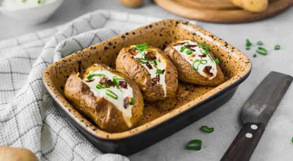 Drei gebackene Kartoffeln im Ofen, gefüllt mit Sour Cream und Speck. Garniert mit Schnittlauch.