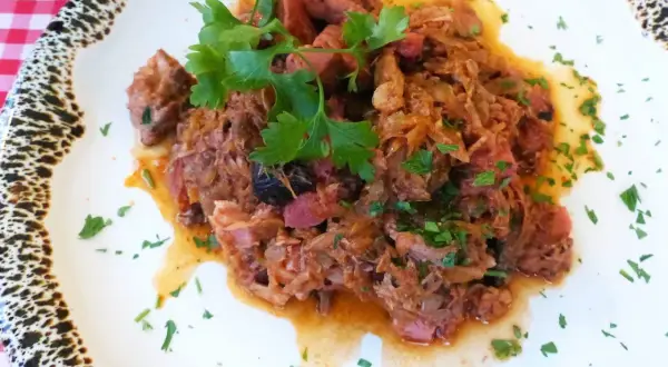 Pyszny bigos z kiszonej kapusty, bogaty w mięso i przyprawy, udekorowany świeżą natką pietruszki.