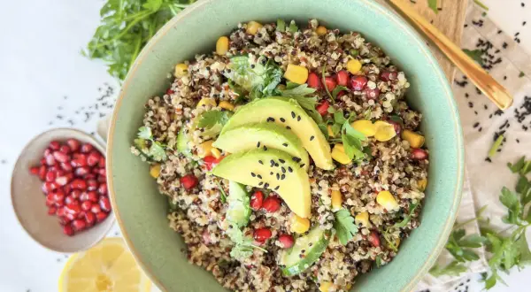 Bunter Quinoa Salat mit Avocado, Granatapfelkernen, Mais und Petersilie, garniert mit schwarzen Sesamkörnchen.