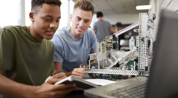 Dos estudiantes trabajan en un robot, aplicando la metodología STEM para resolver un desafío de ingeniería.