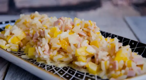 Reissalat mit Mandarinen und Schinken, cremig und fruchtig, auf einem dekorativen Teller serviert.
