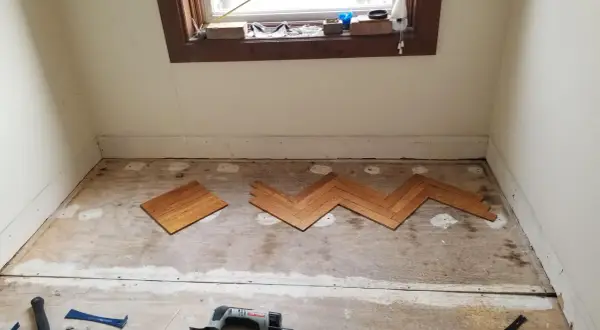 Wooden floor planks laid in a herringbone pattern on a subfloor, tools nearby. This is part of a project on how to level floor.