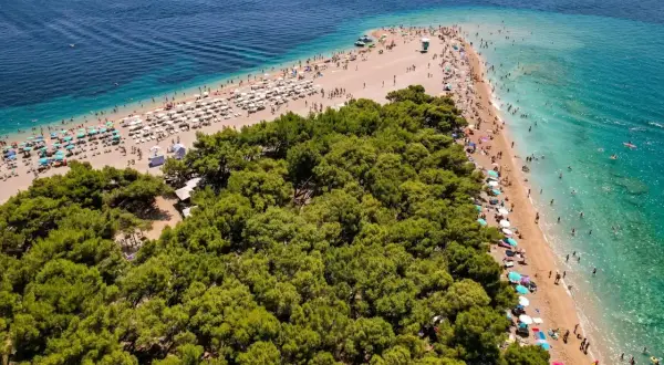 En solig strand med många parasoller och badande människor vid Zlatni Rat, en berömd udde på ön Brač i Kroatien.