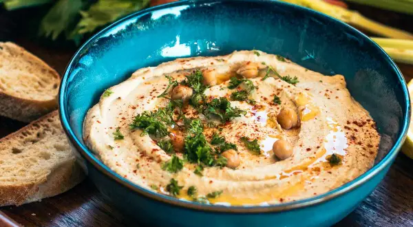 Cremiger Hummus mit Kichererbsen, Petersilie und Paprikapulver in einer blauen Schüssel, serviert mit Brot. Ein köstliches Hummus Rezept.
