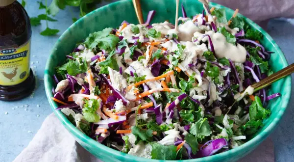 En fräsch kycklingsallad med rödkål, morötter och grönkål, toppad med en krämig dressing. En flaska kycklingfond syns i bakgrunden.