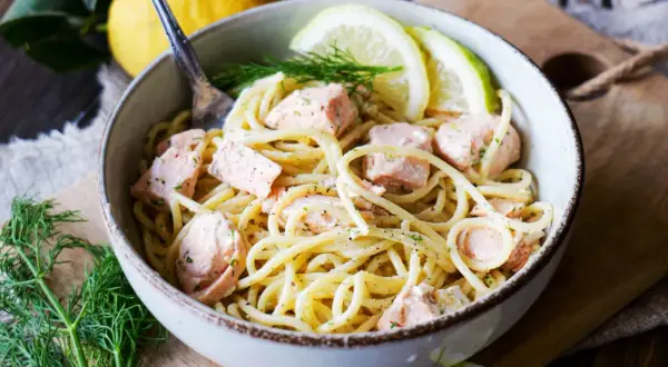 Schüssel mit cremigen Nudeln mit Lachs, garniert mit Zitronenscheiben und Dill. Ein Genuss für Feinschmecker!