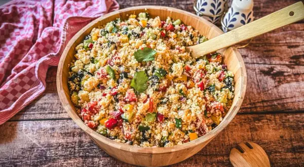 Ein bunter Couscous-Salat mit Feta, Tomaten, Gurken und Paprika, serviert in einer Holzschüssel.