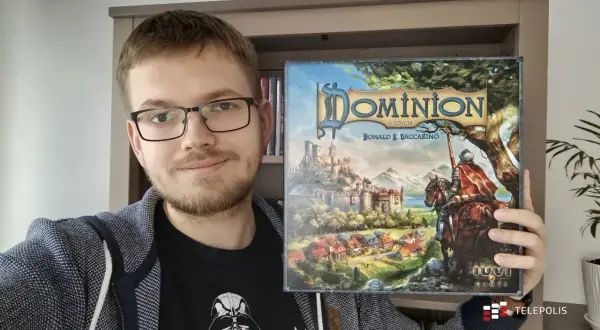Uśmiechnięty mężczyzna prezentuje pudełko gry "Dominion II Edycja". To dopiero początek przygody z nowymi dodatkami!