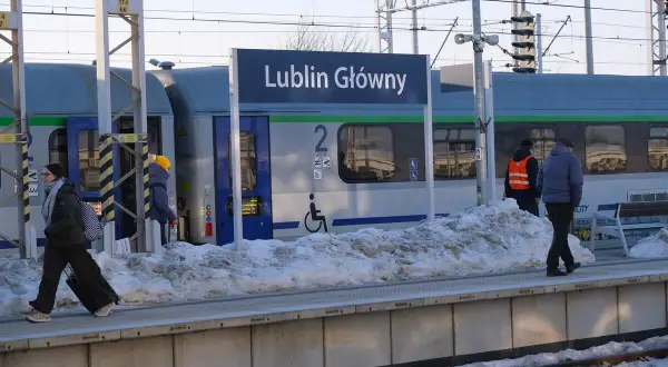 Zimowy dzień na stacji Lublin Główny. Pasażerowie z bagażami czekają na pociąg, a śnieg zalega na peronie.