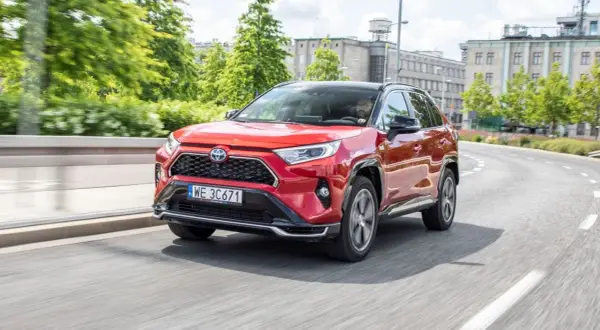 Czerwona Toyota RAV4 Hybrid w ruchu miejskim. Kierowca w okularach za kierownicą. Niskie toyota rav4 spalanie to atut tego SUV-a.