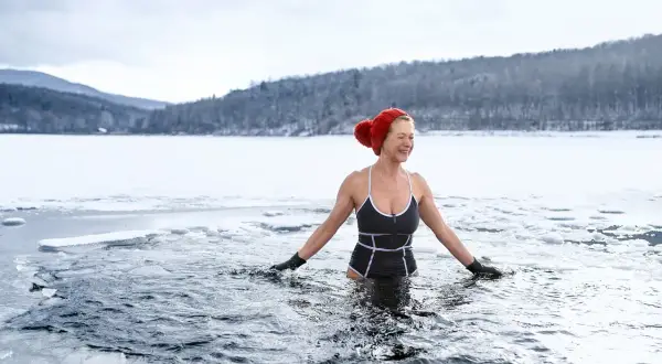 Frau genießt eisbaden in gefrorenem See. Sie lacht und fragt sich, ob eisbaden gesund ist.