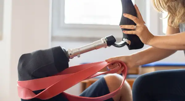 Una donna aiuta a indossare una calza su un moncone gamba protesico, con una fascia rossa in primo piano.