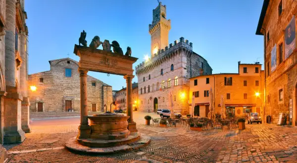 Piazza illuminata a Montepulciano, con pozzo rinascimentale, Palazzo Comunale e chiese. Perfetta per scoprire le cose da fare in zona.