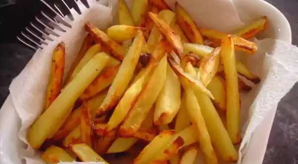 Un plat blanc rempli de délicieuses frites au four, dorées et croustillantes, prêtes à être dégustées. Une fourchette est posée sur le bord.