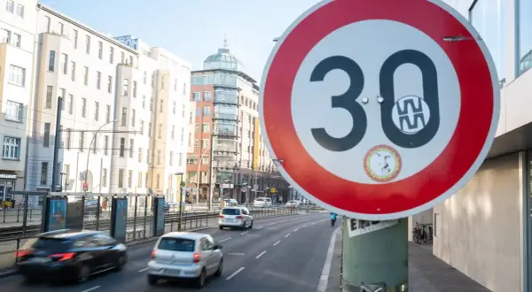 Verkehrsschild "Tempo 30 Berlin" auf einer Straße mit Autos und Gebäuden im Hintergrund.