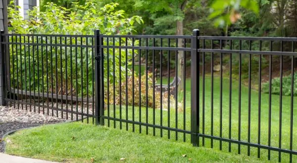 A newly completed metal fence installation encloses a lush green lawn and garden area, providing a sleek and secure boundary.