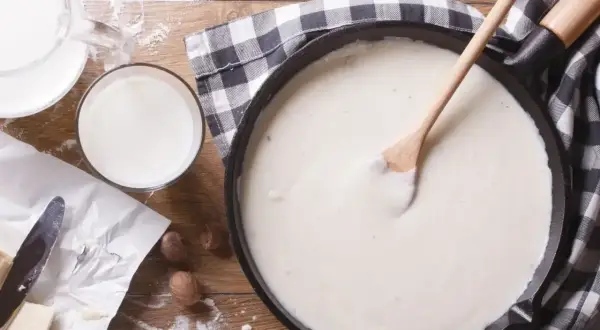 Gładki sos beszamel w patelni, obok mleko, masło i mąka.