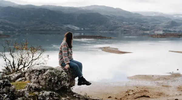 Frau sitzt auf Felsen mit Blick auf einen See und Berge. Ein perfekter Moment während eines Montenegro Roadtrips.
