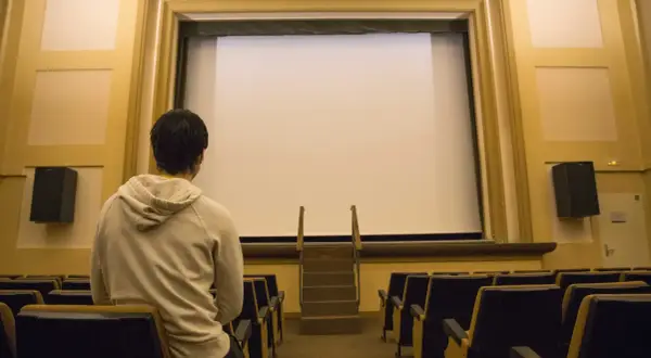 Un joven espera en un cine vacío, listo para disfrutar de una película.