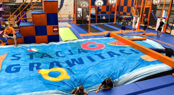 Wesołe skakanie na trampolinach w centrum rozrywki dla dorosłych. Dzieci i młodzież bawią się na wielkiej, niebieskiej macie z motywem basenu.