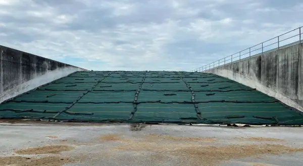 Ampia trincea agricola coperta da telo verde, con pareti in cemento e cielo nuvoloso.