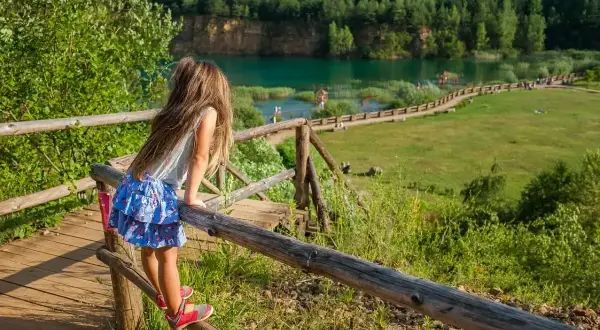 Dziewczynka na drewnianym pomoście podziwia Park Gródek Jaworzno. Cena wstępu jest niska, a widoki zachwycają.