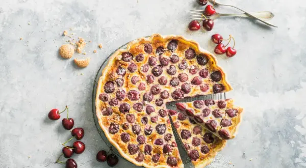 Tarte aux cerises à l'ancienne, garnie de fruits rouges juteux et saupoudrée de sucre glace. Une part est déjà servie.