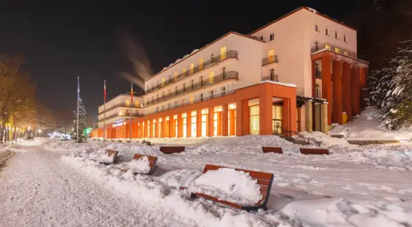 Zimowy wieczór w sanatorium godnym polecenia. Ośnieżone ławki i drzewa tworzą bajkową scenerię.