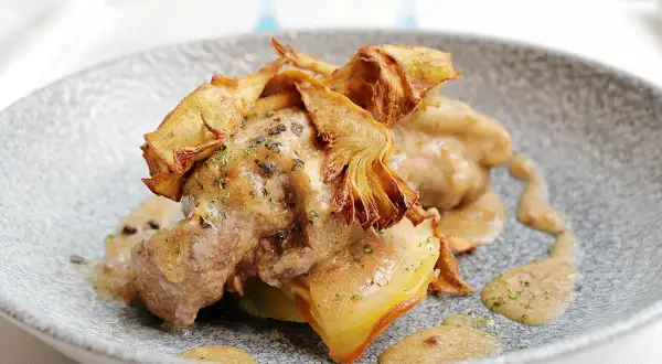 Delicioso ternasco a la pastora, tierno cordero bañado en una rica salsa, coronado con crujientes alcachofas fritas.
