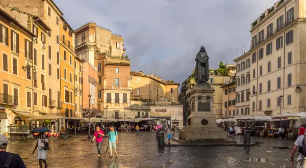 Campo de' Fiori, Rzym. Po deszczu, na mokrym bruku placu, ludzie spacerują obok pomnika.